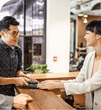 A worker and a customer at a point of sale completing a payment at a terminal with IC card smiling at eachother