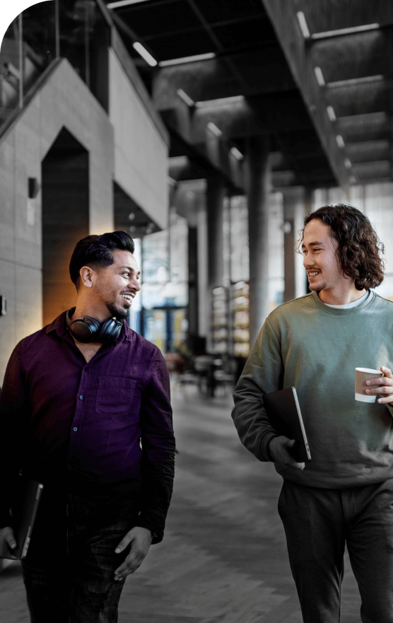 Two young office workers in modern workplace smiling at eachother with laptops in hand